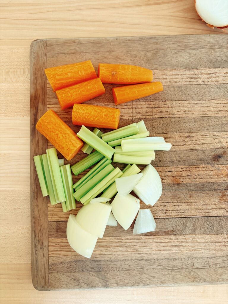 The carrots, celery, and yellow onion roughly chopped and laid out on a cutting board.