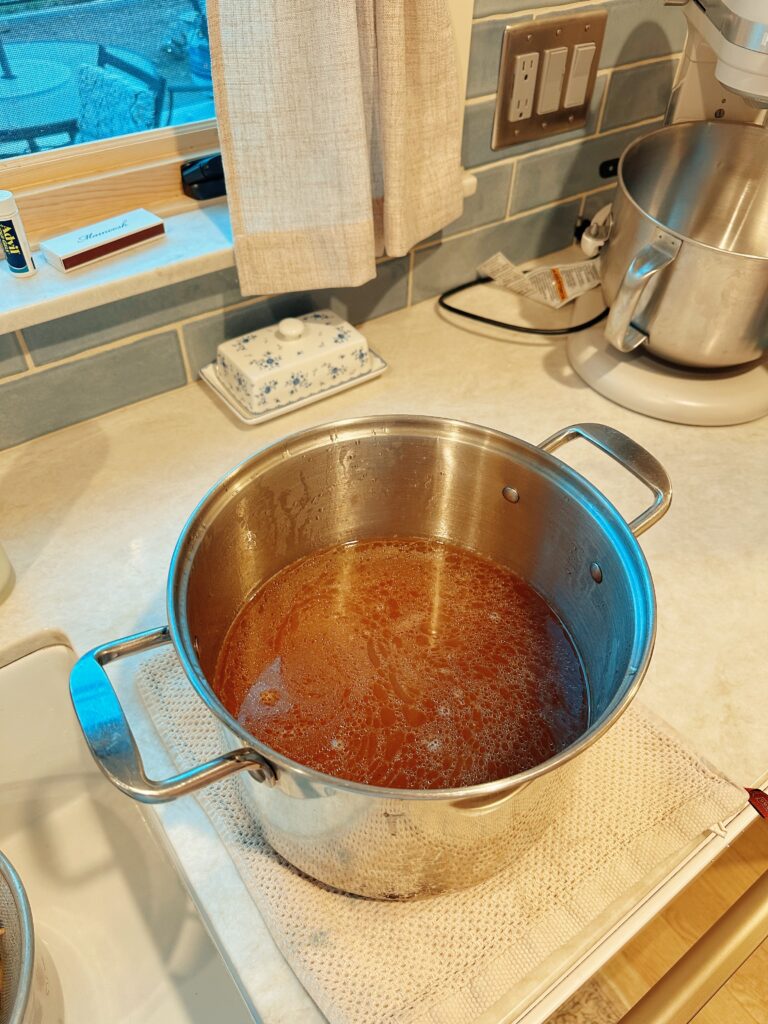 The pot now full of the liquid bone broth is set on the counter atop a towel to cool.