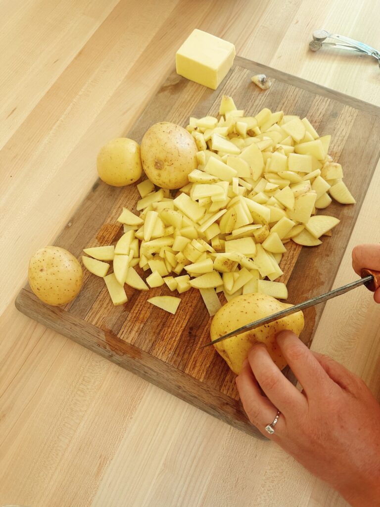 Slicing all of the golden breakfast potatoes into small pieces. They are palaces on top of a wood cutting board wile one is being halved.