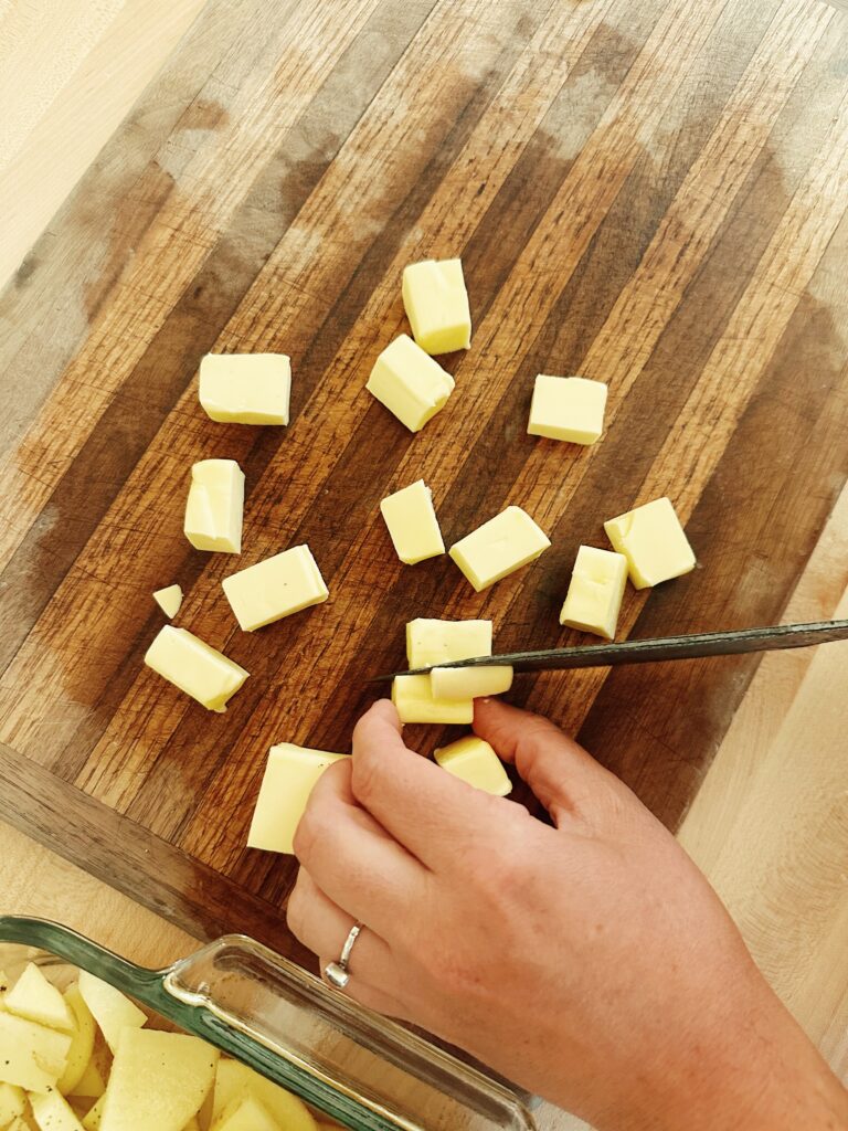 The person is cutting the big block of butter into smaller chunks, that are all places on a wood cutting board.