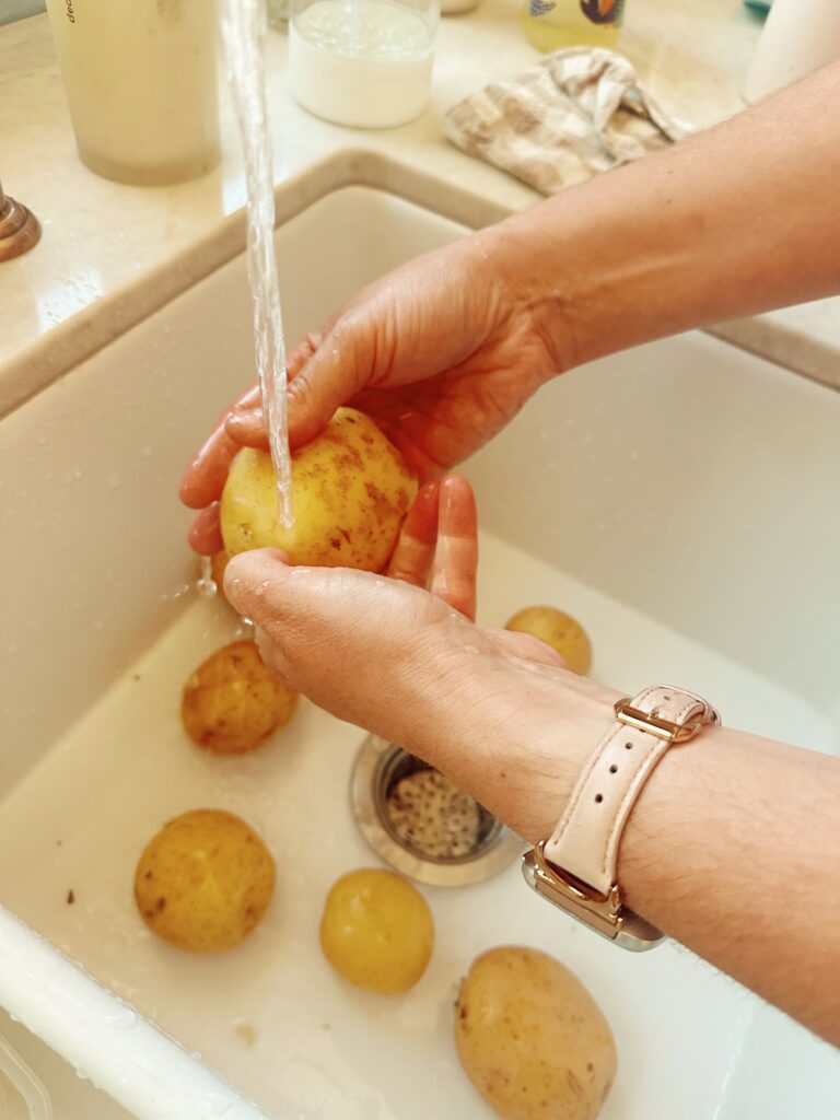 Rinsing all of the golden potatoes in the sink. A person is holding one directly under the water.