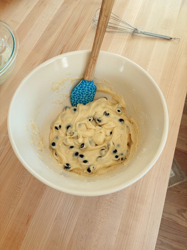 The glass bowl of the combined wet and dry ingredients with blueberries folded in. 