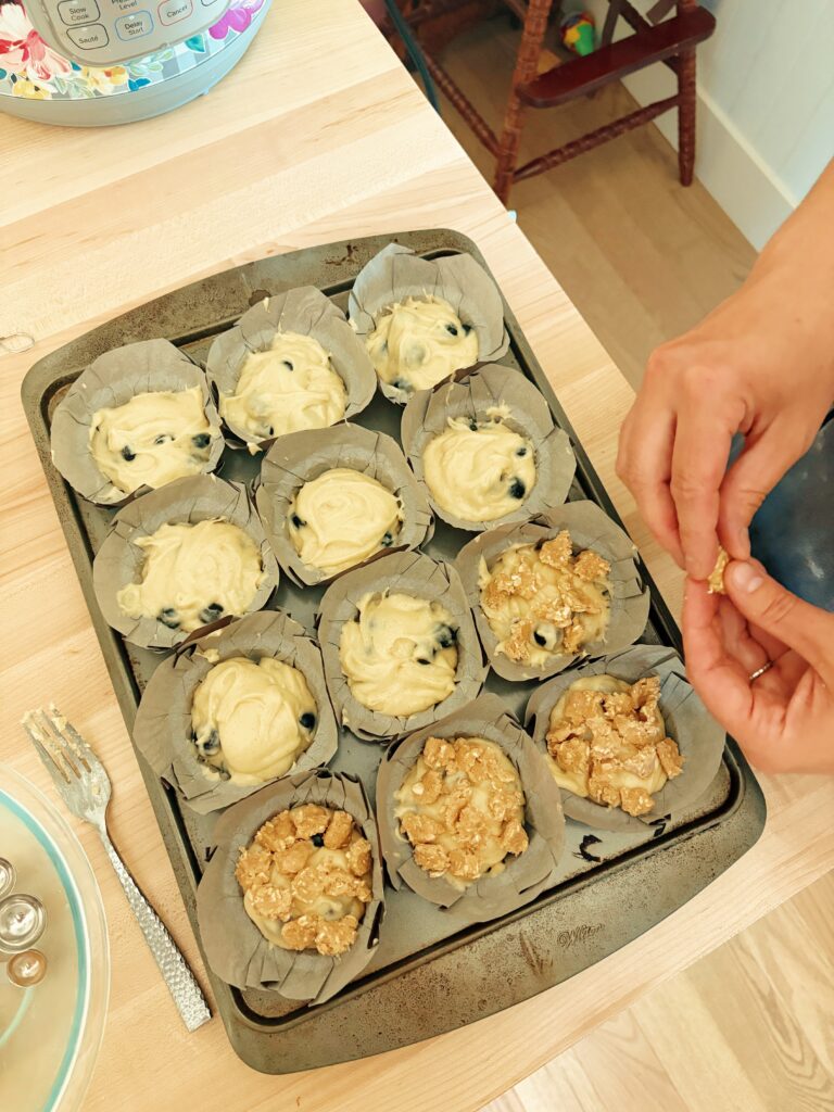 The person is breaking up bits of the crumble mixture and placing them on top of the muffin batter in the tins. 