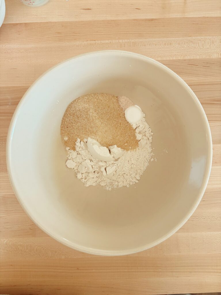 A glass bowl with the dry ingredients inside. Including: flour, baking powder, sugar,  and salt. 