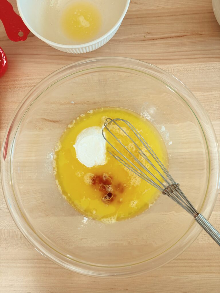 A different glass bowl with the liquid ingredients in it. Including: melted butter, milk, yogurt, and vanilla extract. 