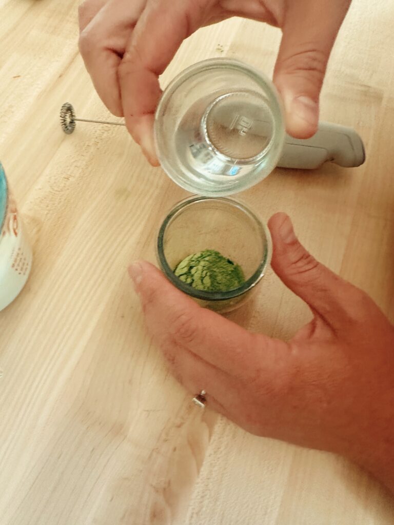 Showing boiling water and matcha latte powder in a small glasses.