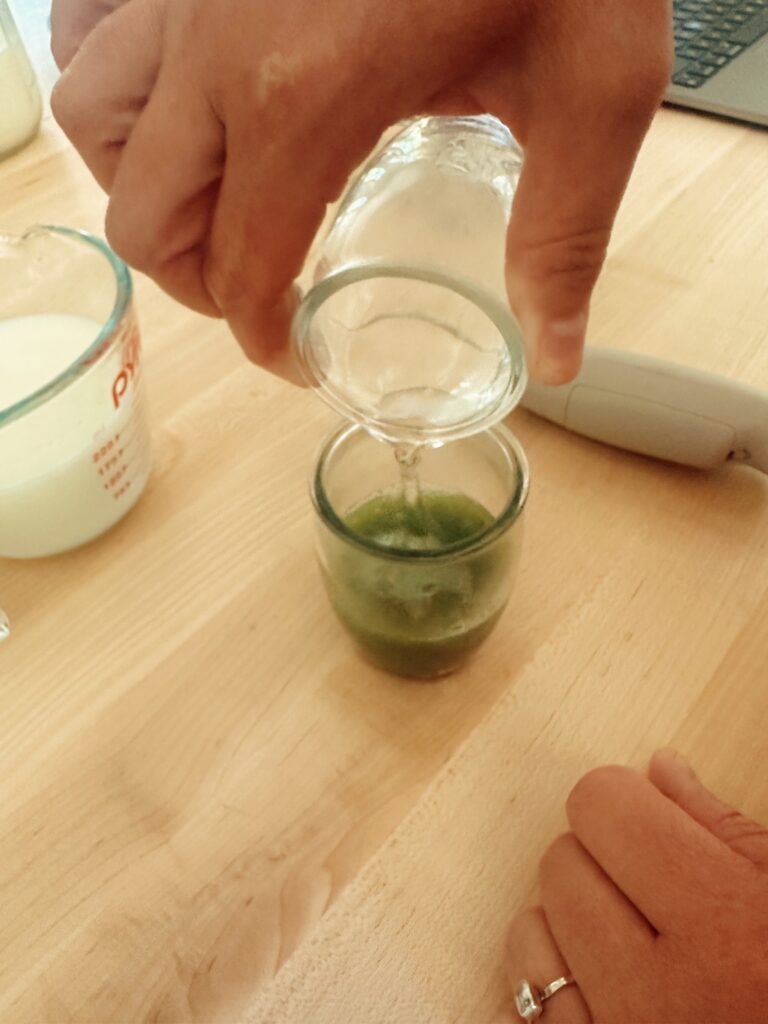 Pouring boiling water into matcha latte powder in small glass.